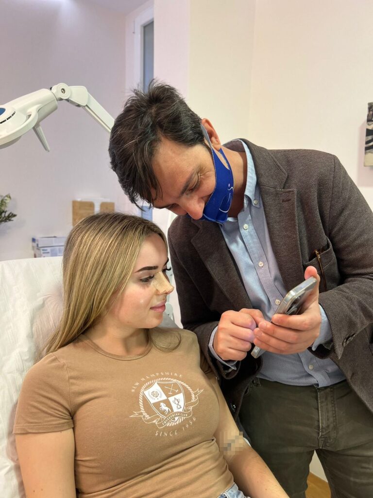 Dr. Gustavo Sordo zeigt einer Patientin ihre Nase auf seinem Mobiltelefon während des Nachuntersuchungstermins 7 Tage nach der Nasenkorrektur.